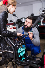 Fototapeta na wymiar Male worker offering help to female customer to repair motorcycle in workshop
