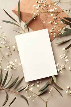 Invitation Or Greeting Card Mockup With Envelope, Eucalyptus And Gypsophila Twigs. Card Mockup With Copy Space On Beige Background.