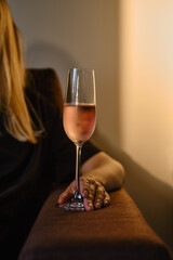 Glass of rose wine in the hands of a girl in the rays of the setting sun at home. Tasting of alcoholic beverages. Celebrate and enjoy the moment. Romantic evening aperitif. Close-up glass of wine