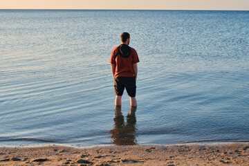 A man stands in the sea or ocean and enjoys the sun on a sunny day. Summer and beach concept. People relaxing in summer. A man traveling. Amazing scenic outdoor view