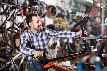 Male is fixing bicycle parts for assembly bike in sports shop.