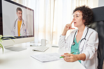 Healthcare worker talking to coworker on video call over computer while sitting at office