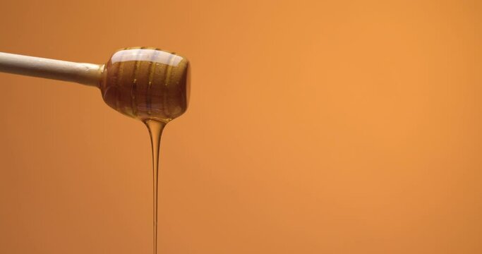 Sweet honey pouring from dipper against color background