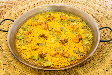 Great and popular Valencian rice paella presented in a paella pan with green flat beans, chunks of stewed chicken, white garrafon beans and a lot of socarrat