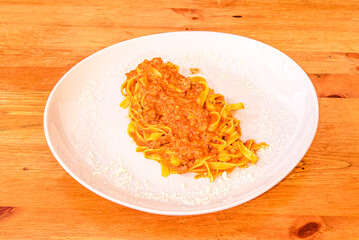 Plate of fettuccine with Italian bolognese sauce and lots of grated parmesan cheese on white plate and wooden table