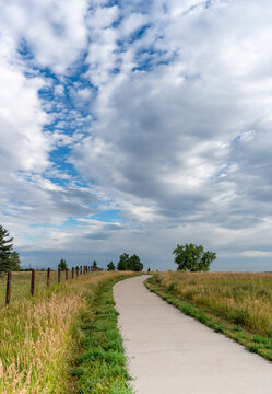 Paved Winding Pathway Along Meadow with Cloud Formations in Sky