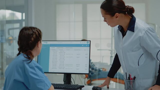 Professional dentist preparing for consultation using x ray from assistant desk at oral clinic. Stomatology nurse working on computer while orthodontist examining patient toothcare