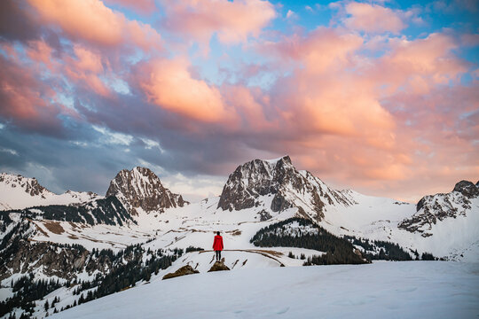Girl in red coat standing in mountainous landscape.