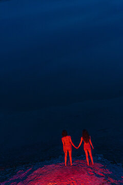 Unrecognizable women holding hands under red light