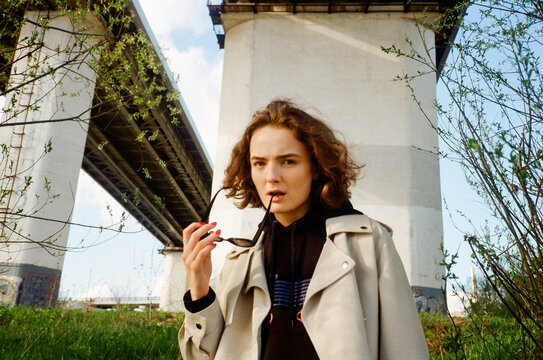 Girl with sunglasses in mouth under a highway bridge