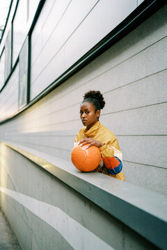Serious female footballer standing with ball in street