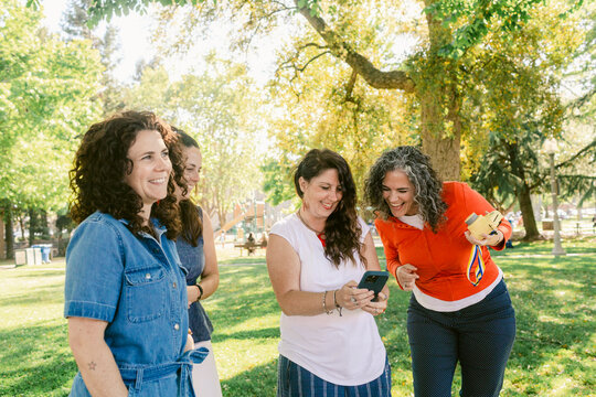 Smiling girlfriends sharing smartphone in summer park