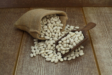 White beans in a bag on a wooden background with space for text. White beans on burlap with wooden spoon