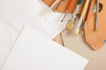 a set of brushes, a wooden palette, white canvas on cardboard and paper on a linen background, artist's workshop concept