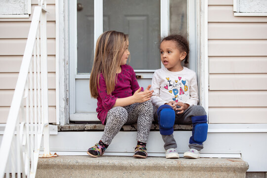 Two children sitting and talking on a houses's top step