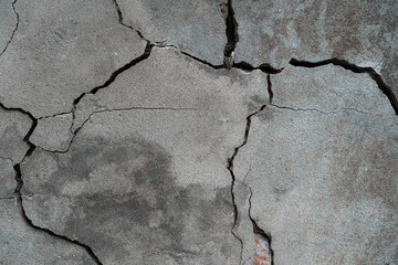 Close up of a cracked concrete wall. Between the cracks you can see the bricks below. 