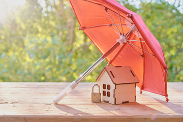 small padlock, red domed umbrella and wooden house model on wooden plank surface, green natural...