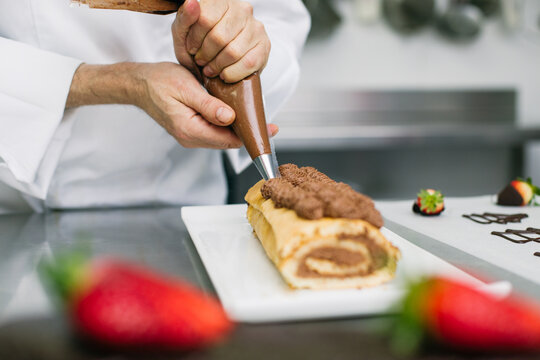 Chef decorating rolled cake with cream 