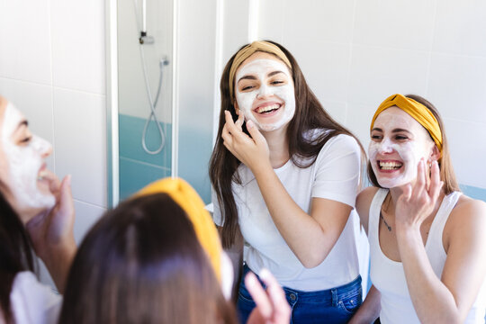 Two girl friends apply clay mask on face at home