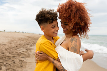Modern redhead mother hugging her son at the beach