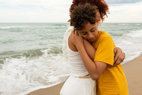 Mother and teenage son hug on the beach