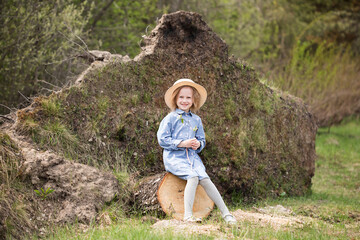 Adorable little caucasian girl sits on a sawn log in the forest