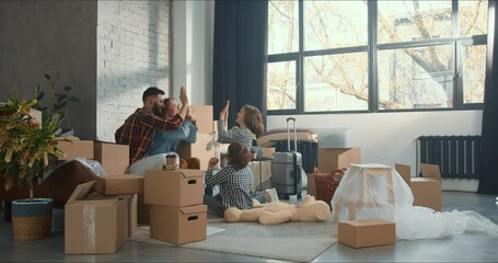 NEW HOME. Young happy family with children sit in light fancy room with boxes after moving in, high five to celebrate.