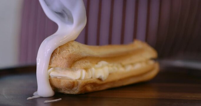 Chef cover the eclair with glaze choux cream. Decorating eclairs with vanilla cream. Glaze on eclair and profiteroles. Freshly baked crispy oblong eclairs. Traditional French eclairs with custard.