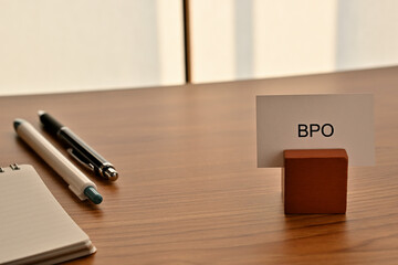 There is a card on paper stand with the word of BPO which is an abbreviation for Business Process Outsourcing on the desk with a pen.