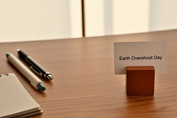 There is a card on paper stand with the word of Earth Overshoot Day on the desk with a pen.