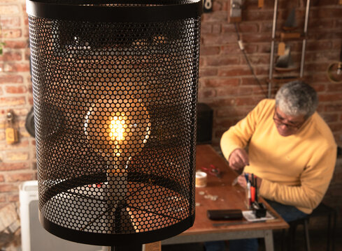 Primer plano de una lámpara encendida en una tienda y se ve a un hombre trabajando en su escritorio