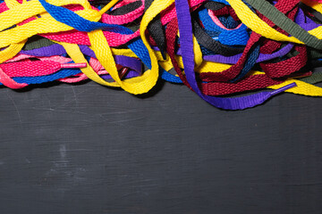colorful shoelaces background, on black wood, messy, clutter concept, advertisement