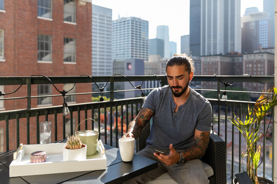 Man Sitting on Balcony Uses Phone