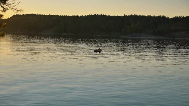 silhouette of person with little child sailing small kayak along large tranquil lake against dark forest at bright sunset