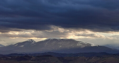 Fototapeta na wymiar Nuvole tempestose sopra le montagne e raggi di sole al tramonto