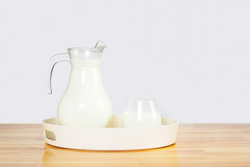 milk in a glass and a jug on a wooden table in a round tray on a gray background. copy space..