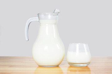 milk in a glass and a jug on a wooden table on a gray background. copy space..