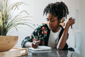 Black teenager listening to music and taking notes in notebook