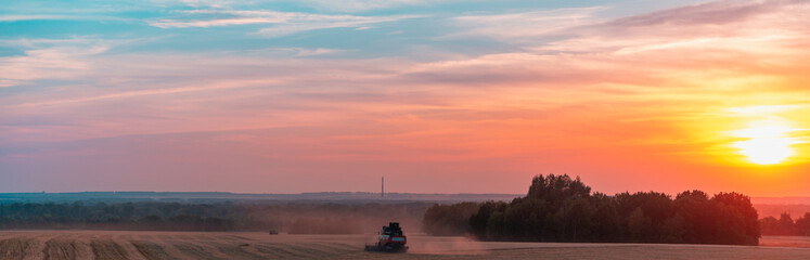 Obraz premium Harvester harvests in a field at sunset.