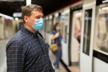 Portrait of male passenger in disposable face mask and latex gloves waiting for train on subway...