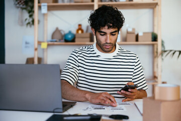Hispanic employee with smartphone examining bar codes