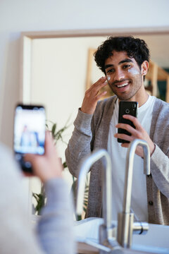 Cheerful man applying cream and shooting video