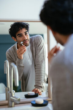 Hispanic man with jade roller looking at mirror