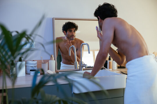 Shirtless guy looking at mirror and cleansing face