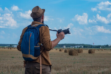 Traveler photographer with a camera in his hand against the background of a field and haystacks.