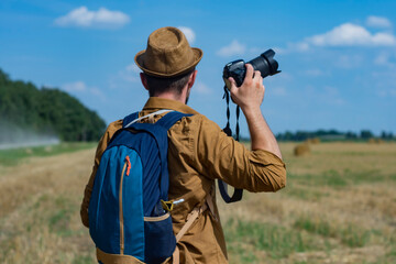 Traveler photographer with a camera in his hand against the background of a field and haystacks.