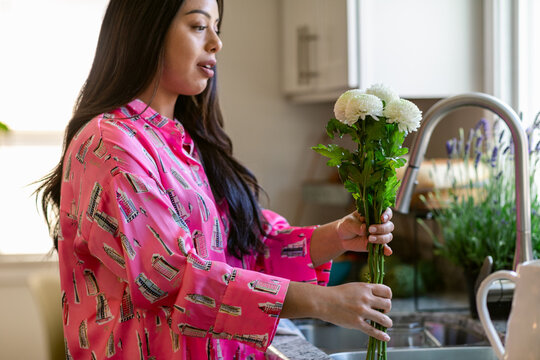 Woman arranging floral bouquet near sink in home kitchen