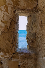 A view of the sea through the loophole of a medieval fort in the southern part of the Finikoudes embankment on the island of Cyprus. The fort is located in the city of Larnaca.