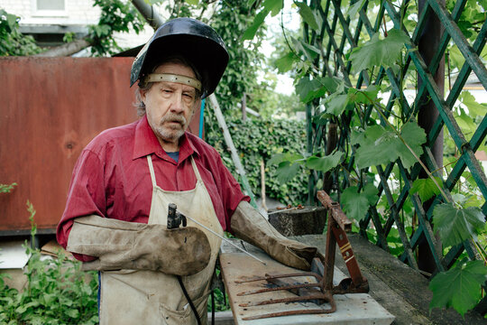Senior male welder in apron working in backyard