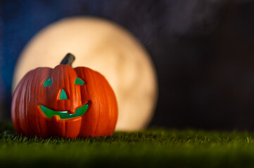 Halloween holiday. On the green grass, a pumpkin in the form of a head against the background of a dark blue sky and a large white moon. Cloudy sky. Night. Halloween, holiday, October.